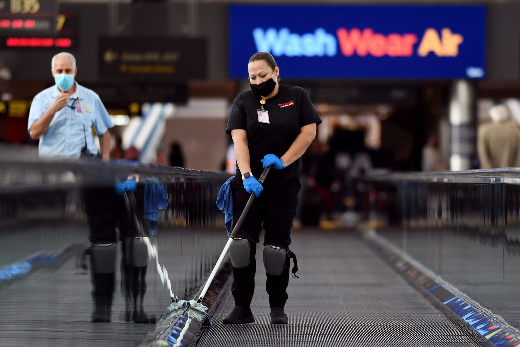 Photo shows a woman cleaning a moving walkway in an airport concourse.