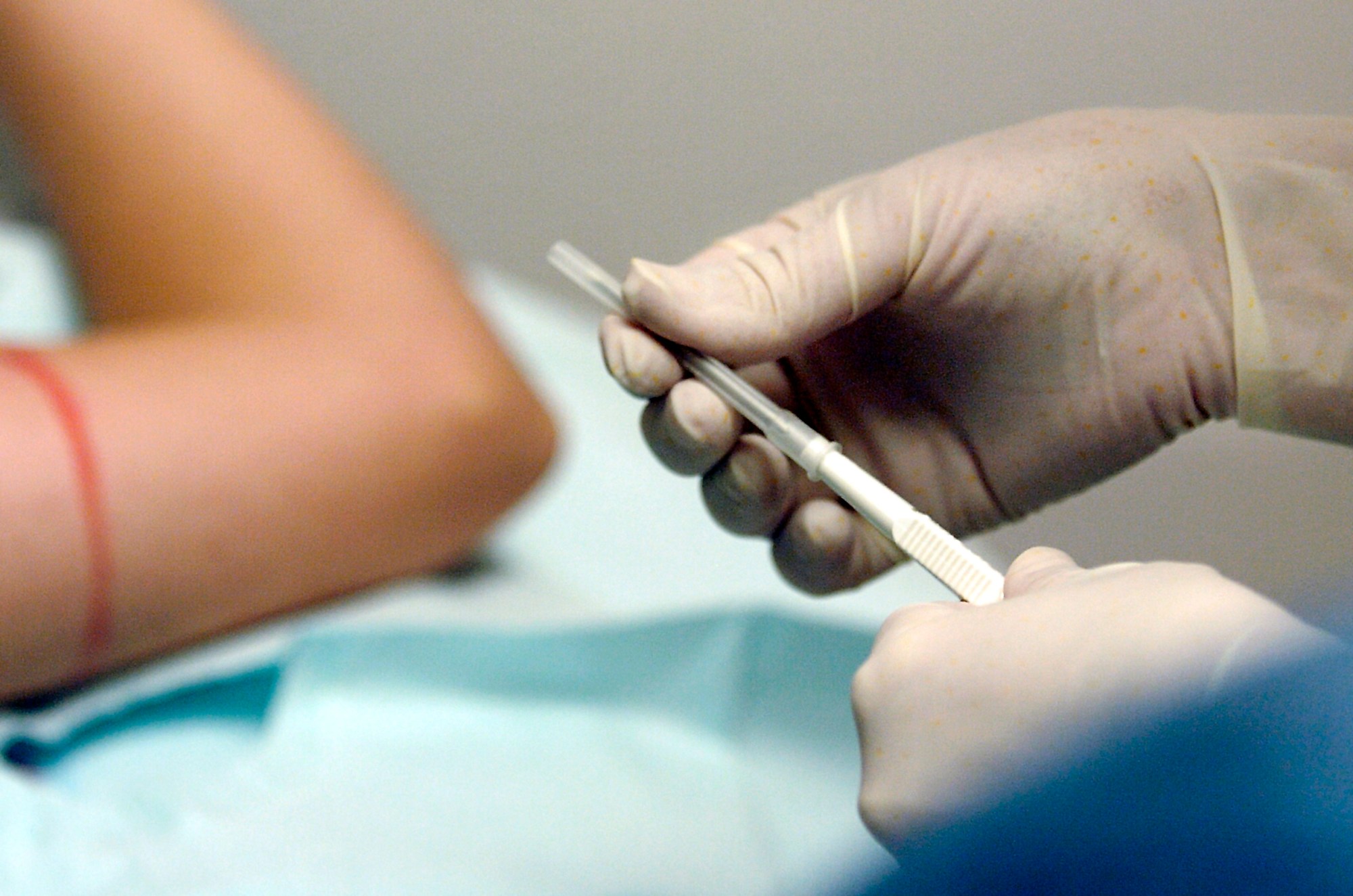 In a close-up shot, a nurse's gloved hands hold a single-use needle to implant the birth control device in the patient's prepped arm.
