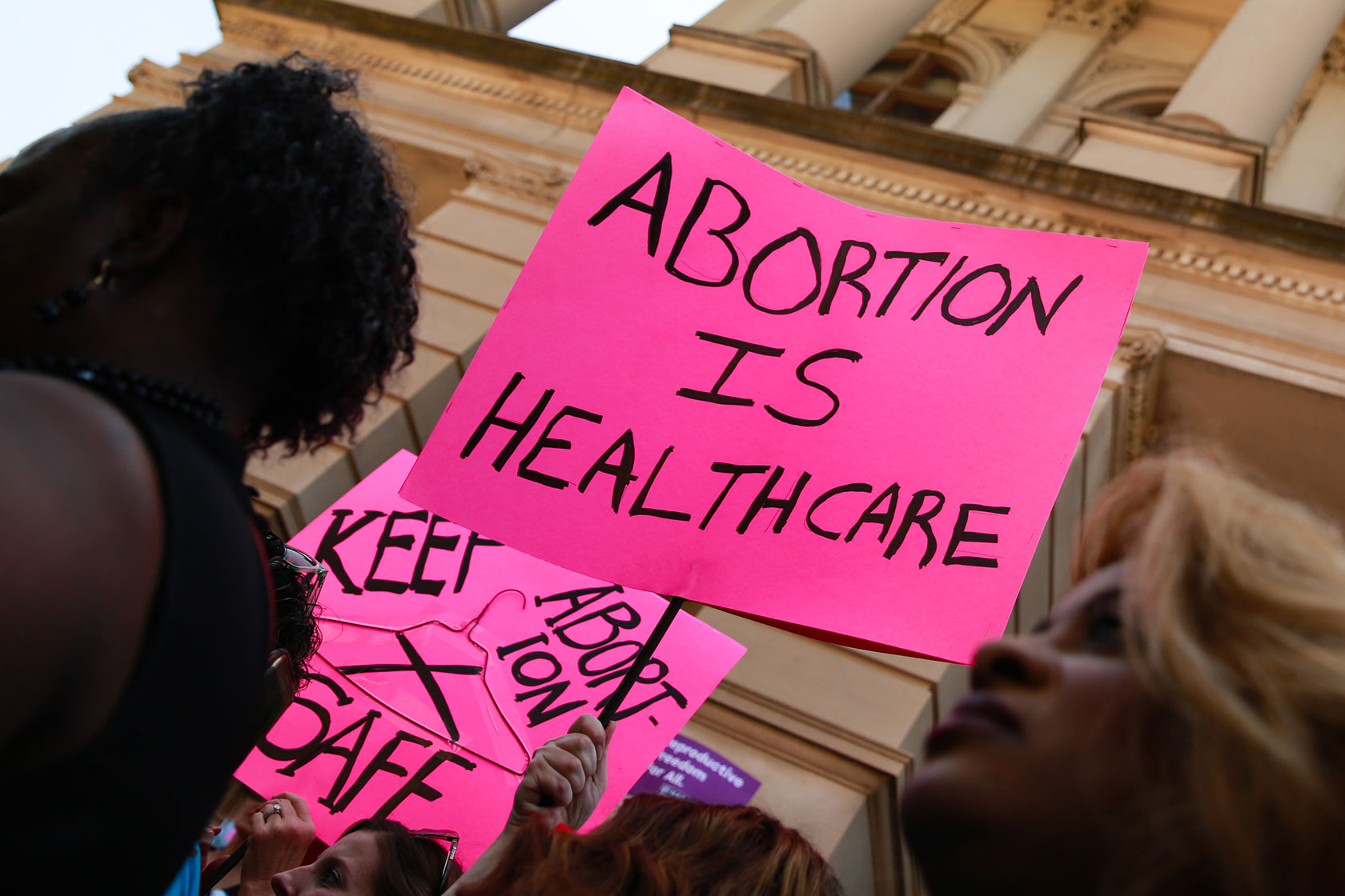 Photo shows protestors holding a bright-pink signs that reads 