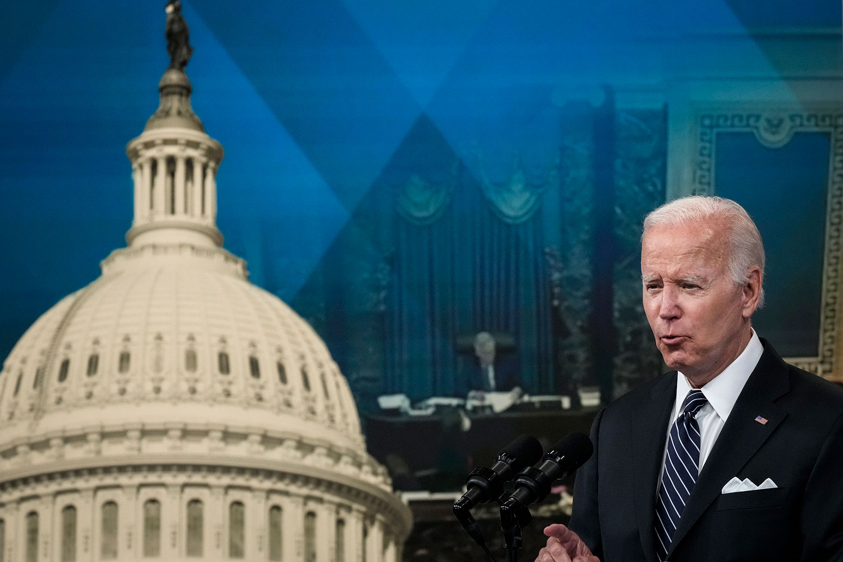 Photo shows Joe Biden standing in front of a large poster featuring the U.S. Capitol dome.