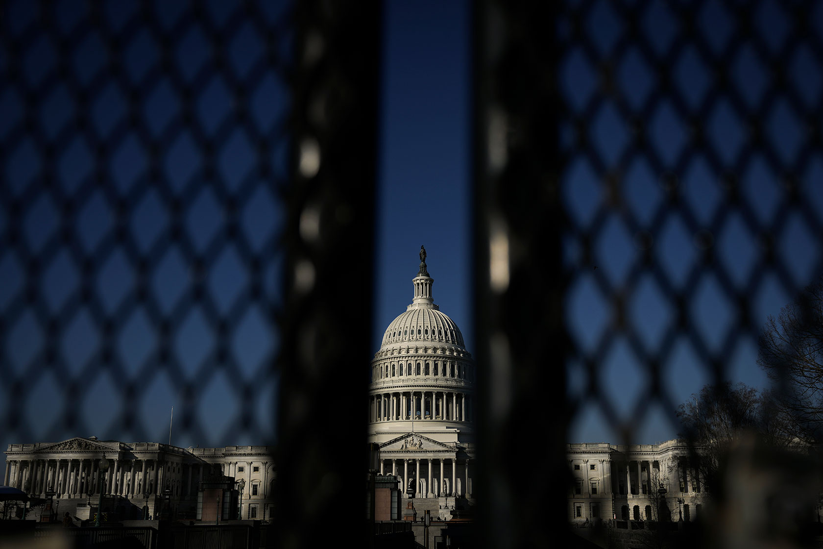 Photo shows the Capitol building dome behind black fencing against a blue sky