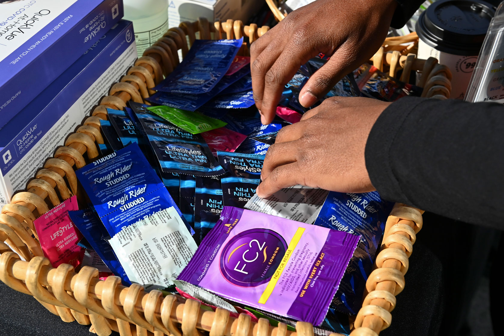 Two hands rifle through a basket with free condoms.