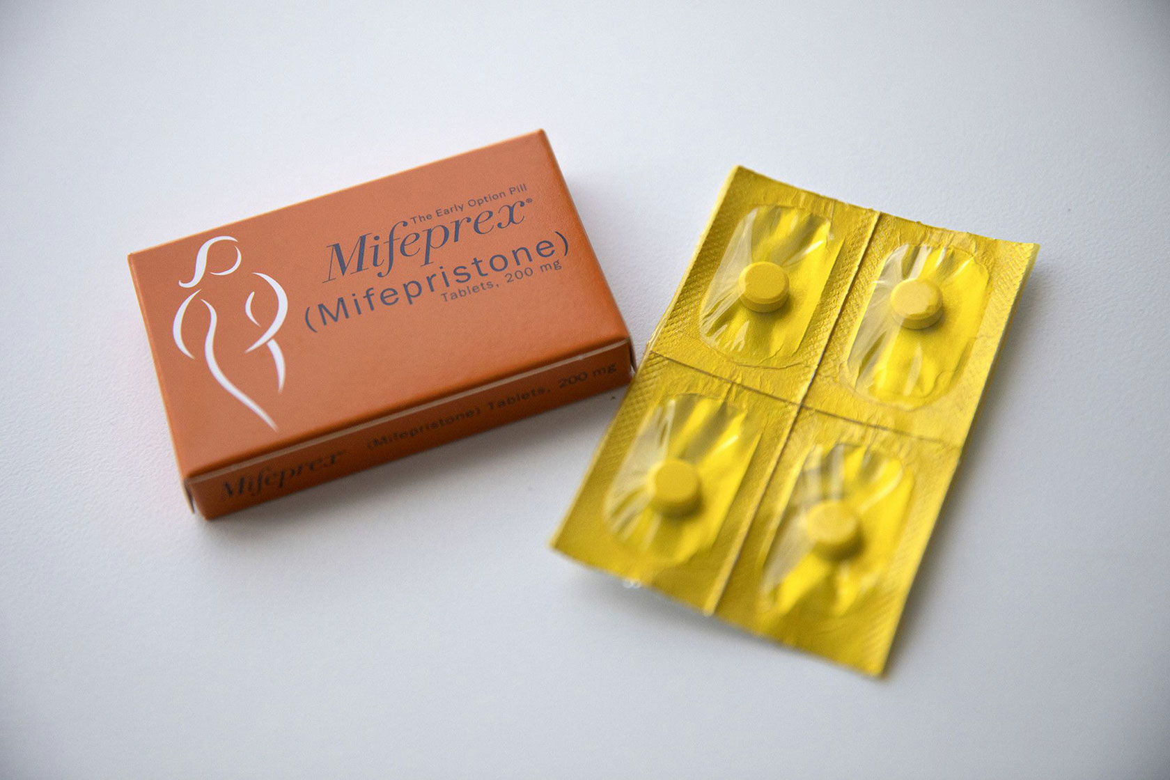 Photo shows an orange box of mifepristone pills next to a yellow container with four pills