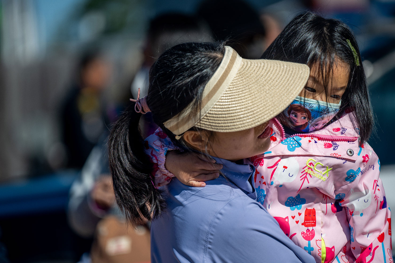 Image showing a mother wearing a visor as she holds a child, who has a face mask on.