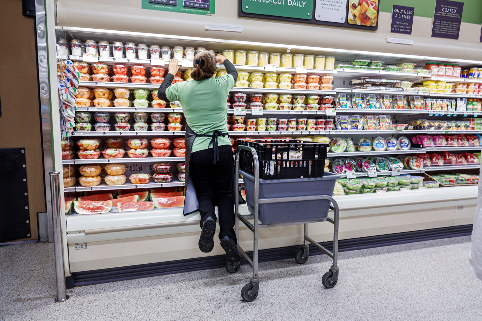 Image showing a female grocery store employee putting pre-cut fruit onto a shelf.