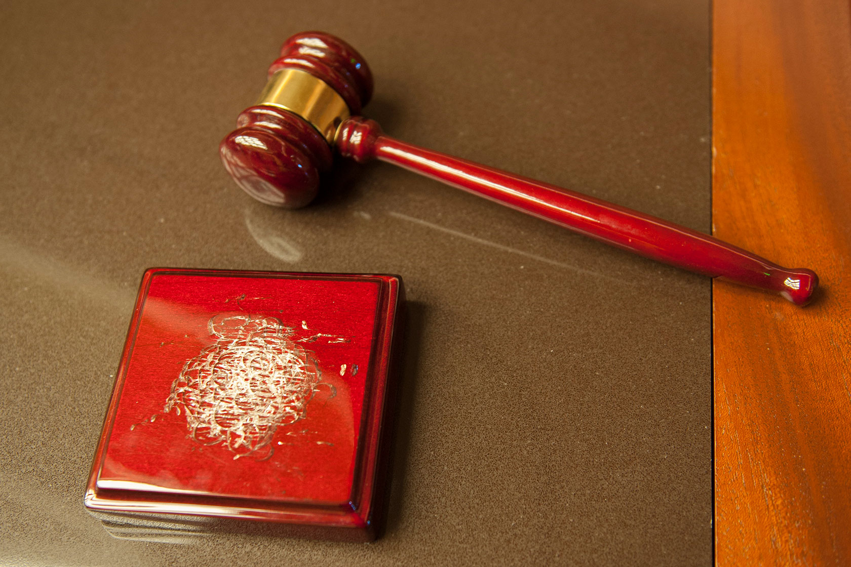 Photo shows a red gavel sitting next to a block with a worn spot where the gavel has struck it over the years