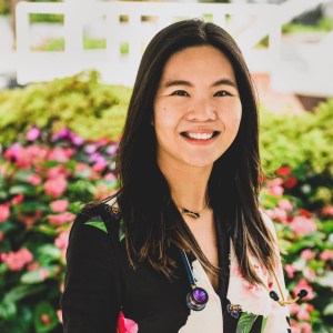 Photo shows Stephanie Liou posing for a headshot wearing a floral shirt against a floral background, smiling at the camera