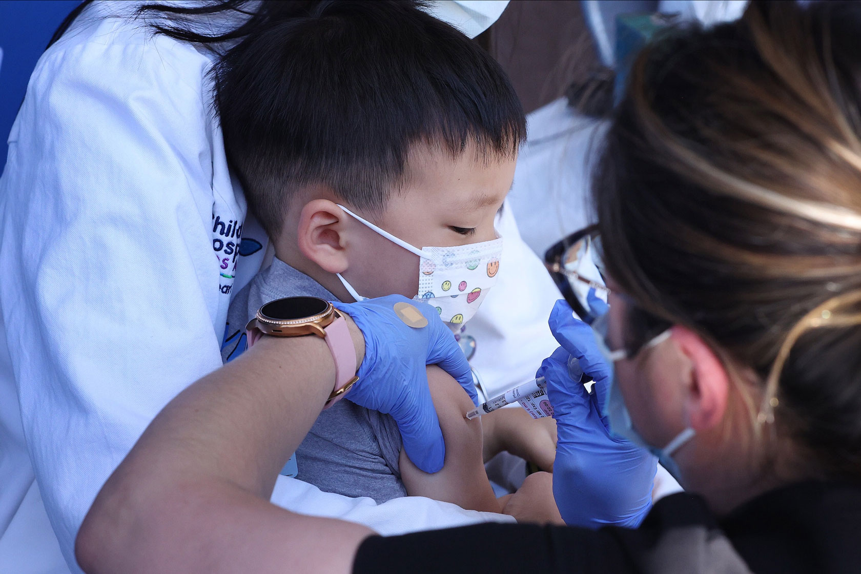 A doctor administers a vaccine shot to a child wearing a mask.