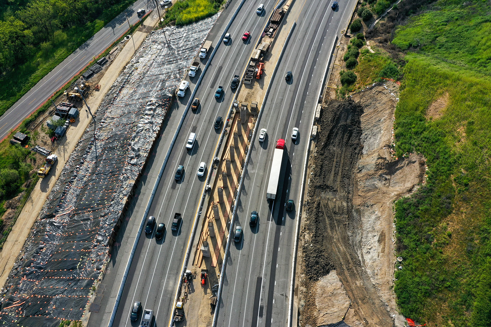 Photo shows an aerial shot of several highway lanes laid down amid rural open land, with cars and trucks driving on both sides