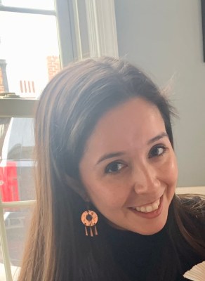 Liz Bastias-Butler smiles for a selfie wearing gold earrings and a black top