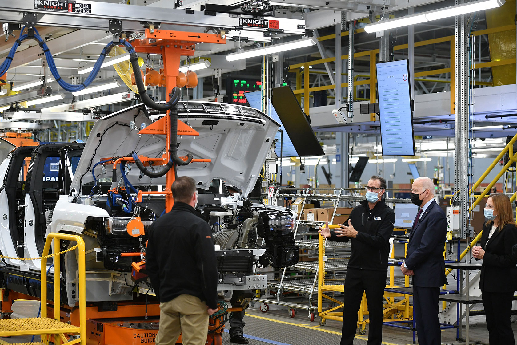 Photo shows Joe Biden standing alongside three other people surrounded by various car parts