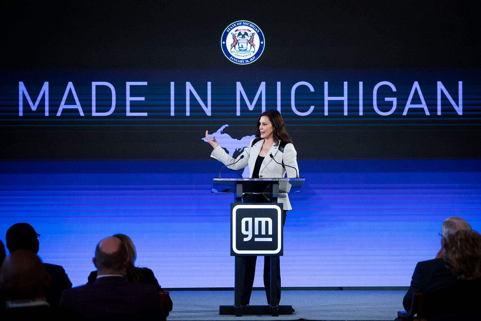 Photo shows Whitmer speaking in front of a large screen that reads 