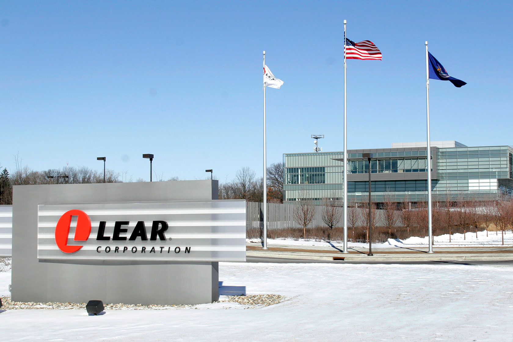 Photo shows the Lear Corp. sign in front of a glass building with three flags flying in front of it, and snow on the ground