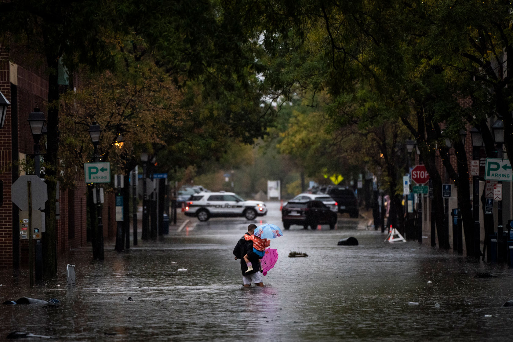 A man holding children walks in the middle of a flooded street.