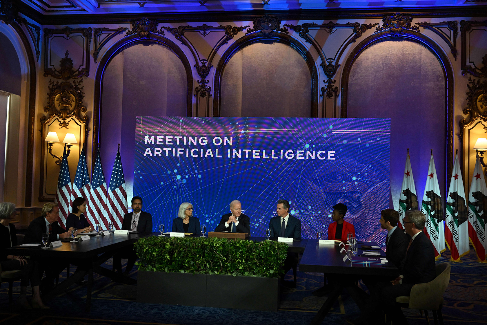 President Joe Biden sits with a panel before a banner that reads, 