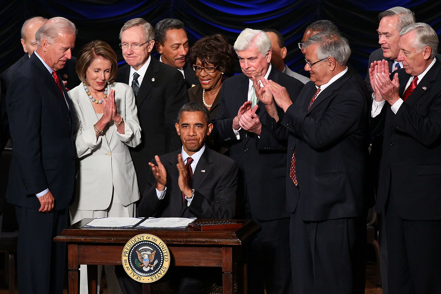 President Barack Obama signing act, surrounded by lawmakers