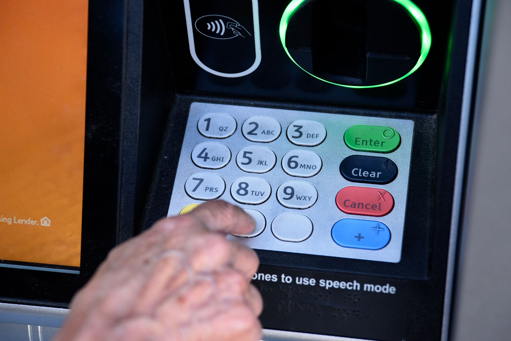 Photo shows a closeup of a hand typing numbers into an ATM machine