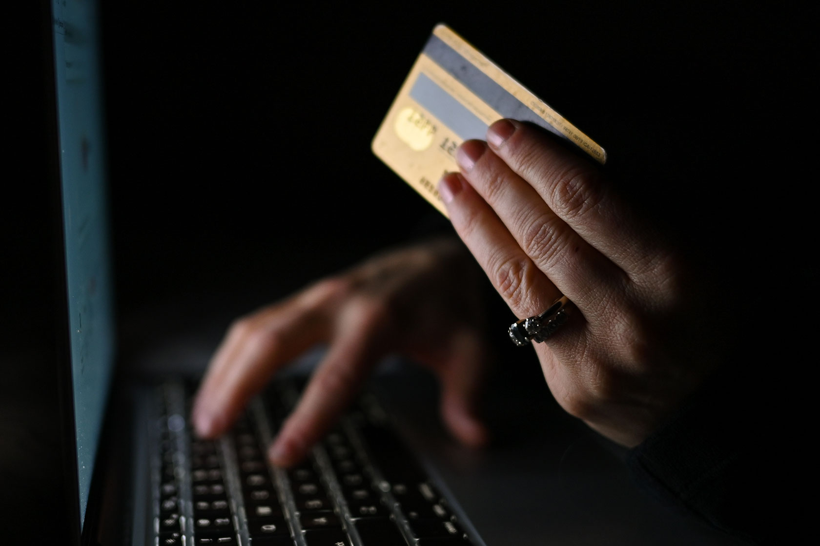 Photo shows a closeup of a hand holding a credit card in front of a laptop