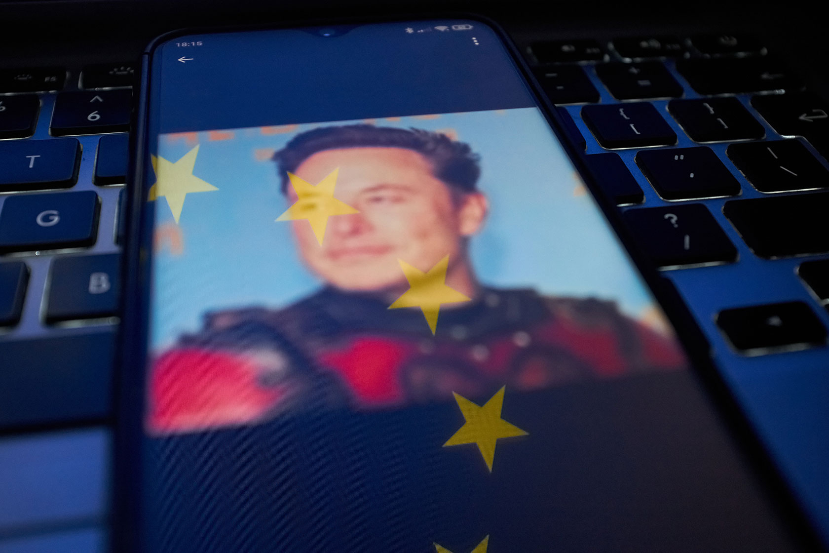 Photo illustration shows Elon Musk's face with the EU flag overlaid, on a smart phone sitting on a keyboard