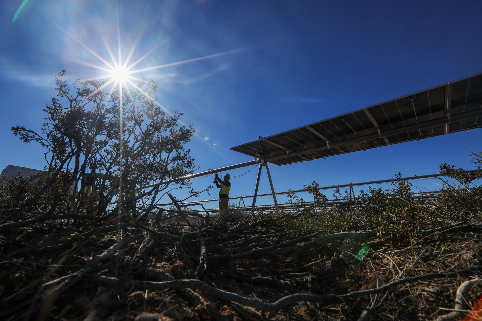 A man works with the wiring at a solar panel installation construction site on a bright, sunny day.