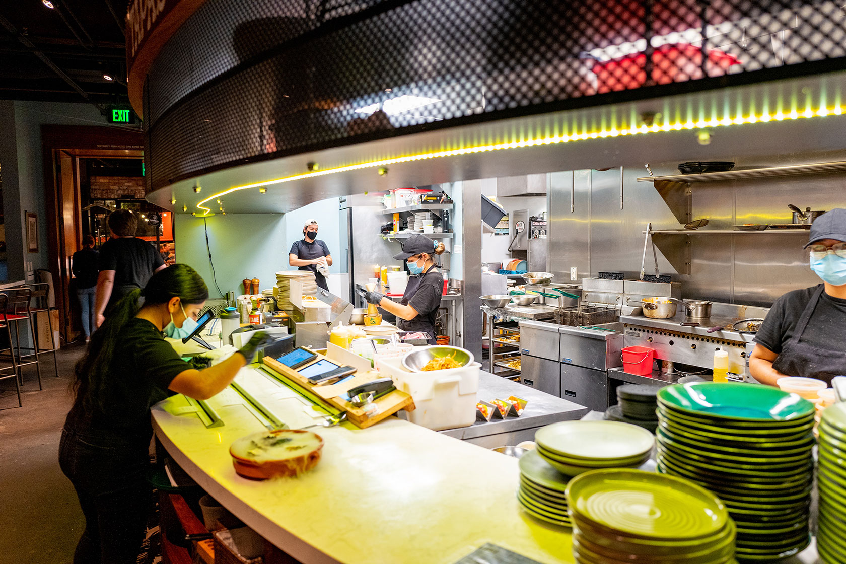 Photo shows a well-lit open kitchen area with chefs preparing food behind the counter and a server picking up plates