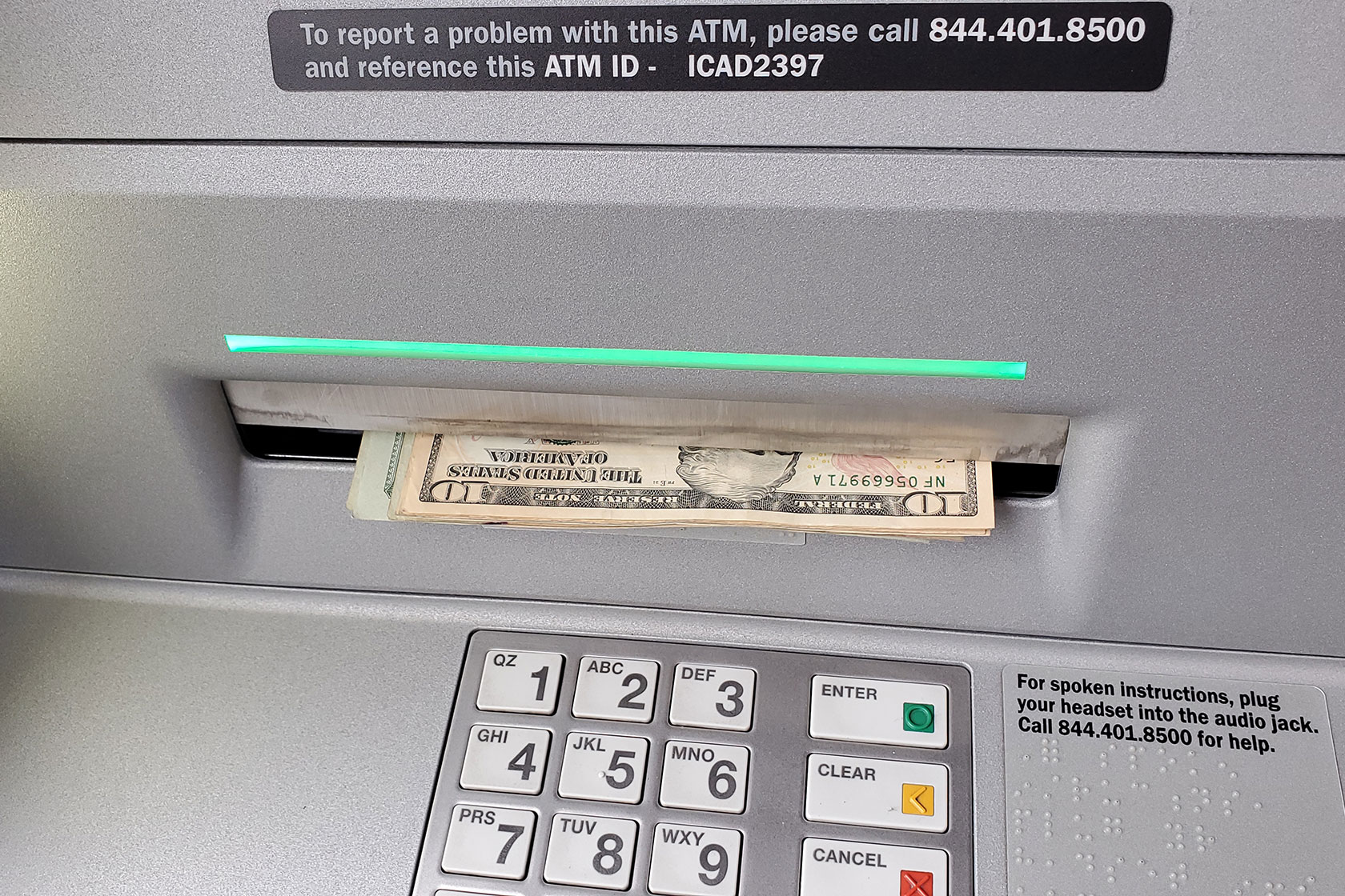 Photo shows a closeup of an ATM dispensing cash above the keypad