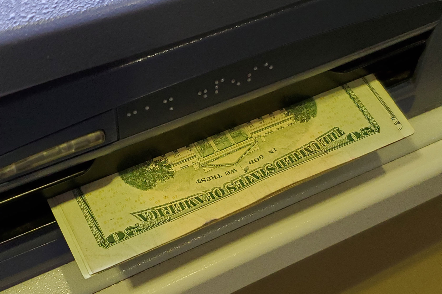 Photo shows a closeup of an ATM slot dispenses $20 bills