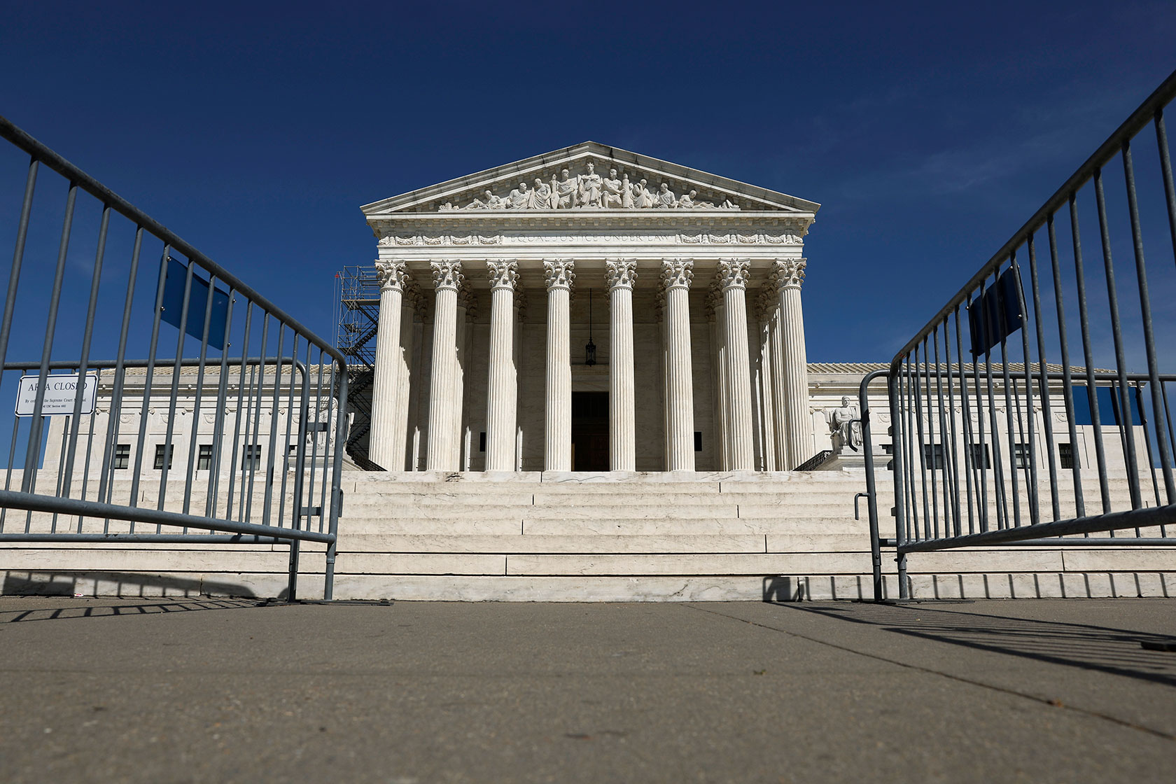 Photo shows the Supreme Court building with fencing in the foreground against a sunny blue sky