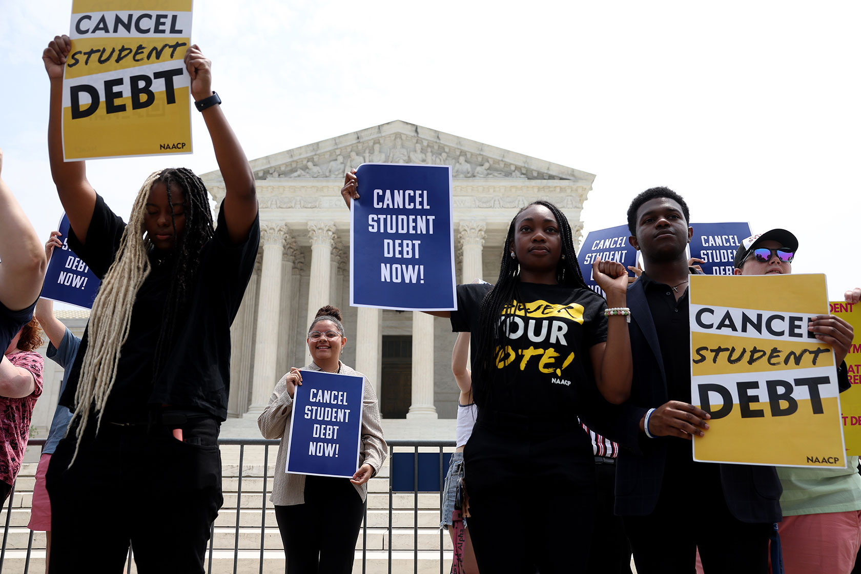 Photo shows people standing in front of the U.S. Supreme Court building holding signs that say 