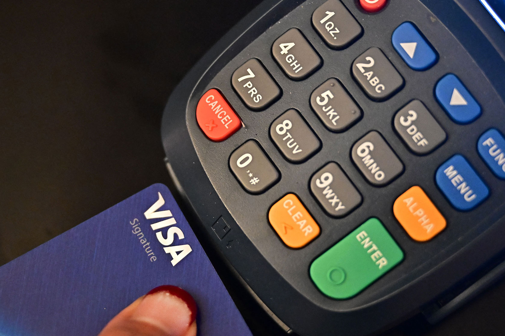 Photo shows a closeup of a person's hand holding a credit card in front of a payment processing machine with numbers and buttons