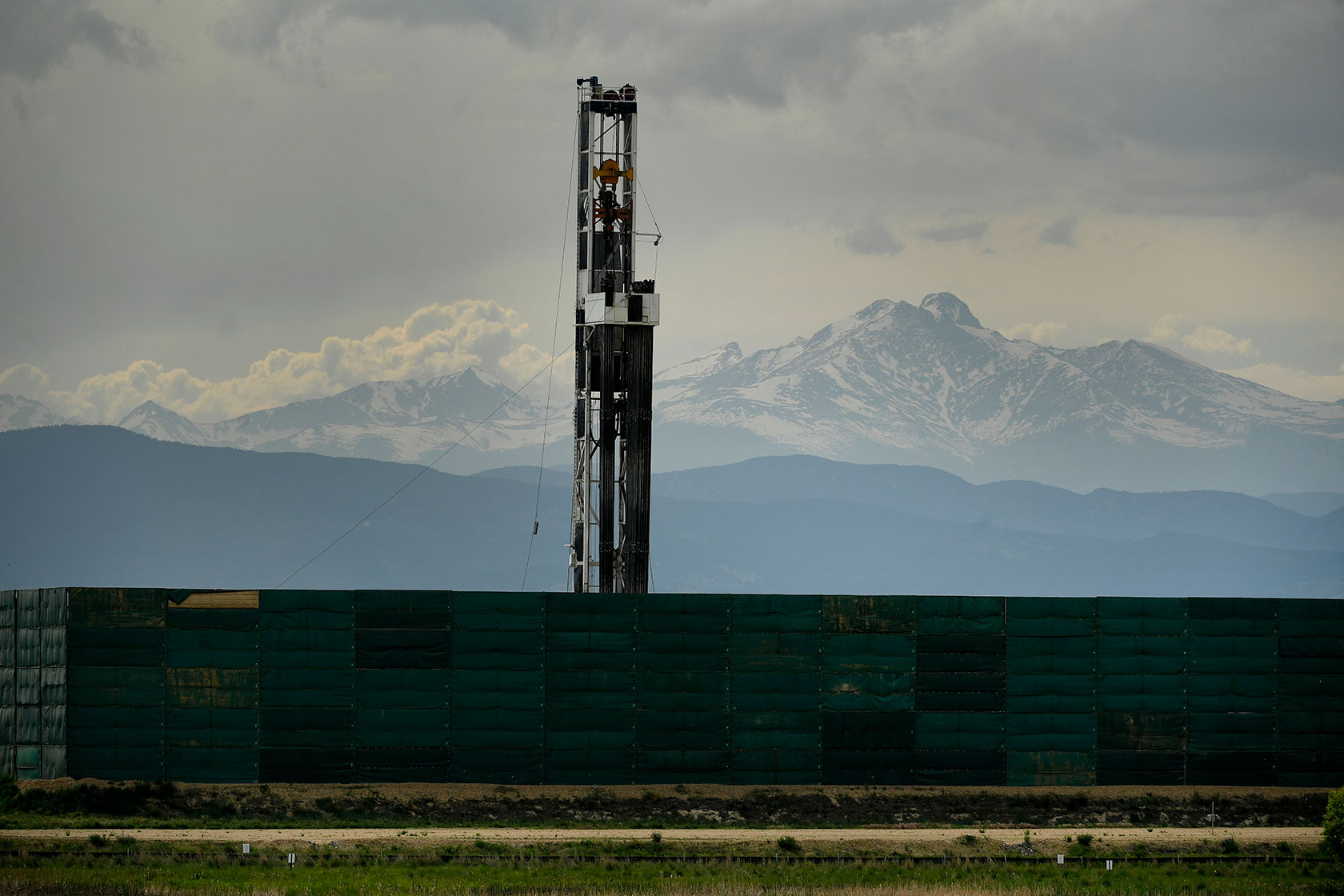 Photo shows drilling machinery with snow-covered mountains and clouds in the background