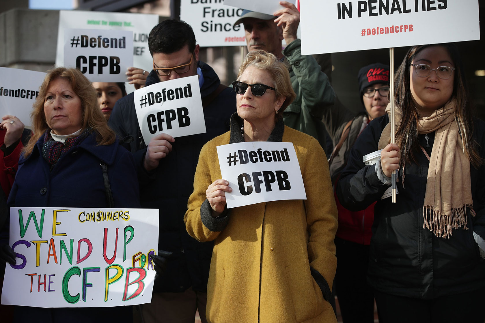 Supporters of the CFPB hold signs that read, “Defend CFPB” outside the agency’s building.