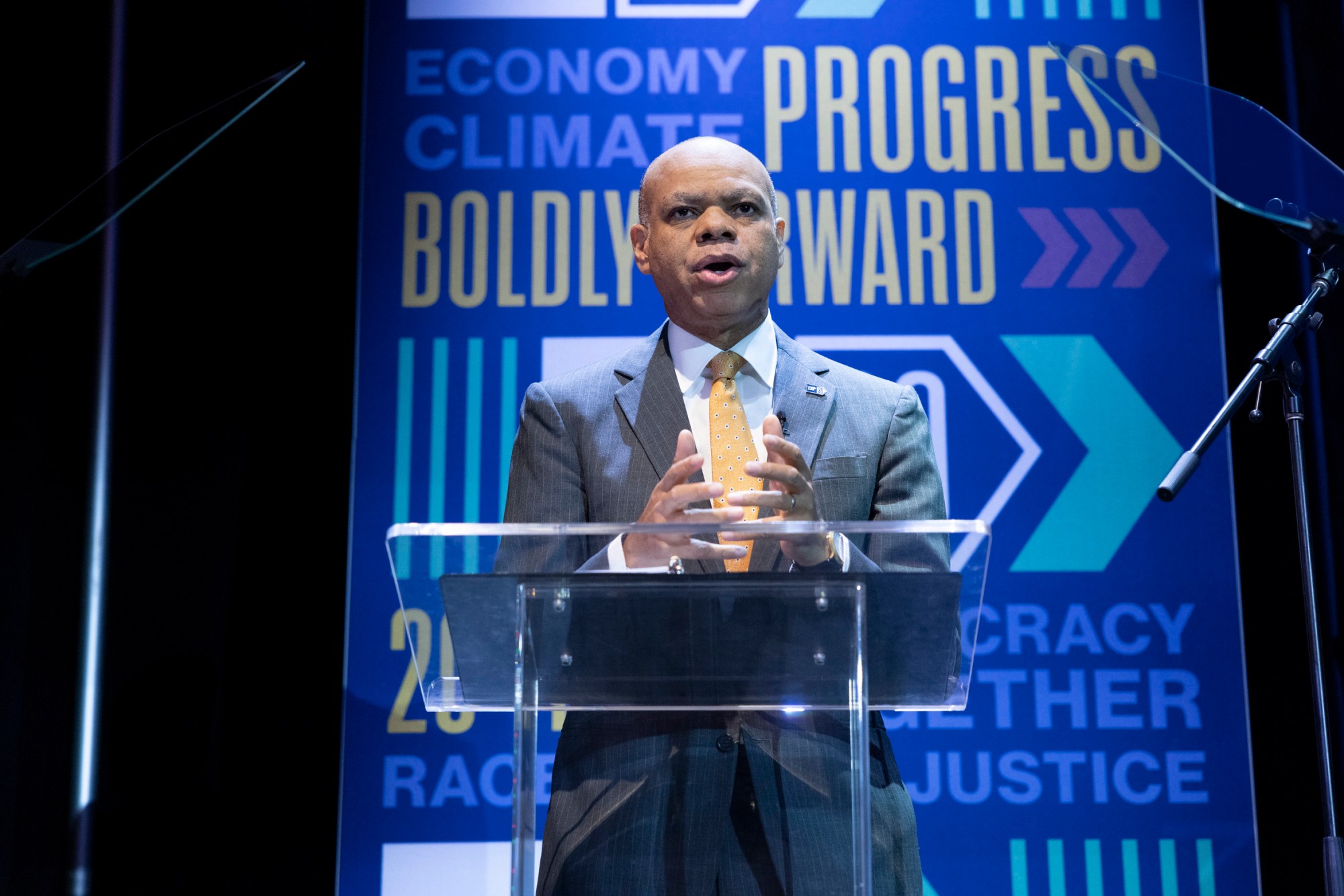 Patrick Gaspard speaks in front of a podium with IDEAS Conference signage in the background