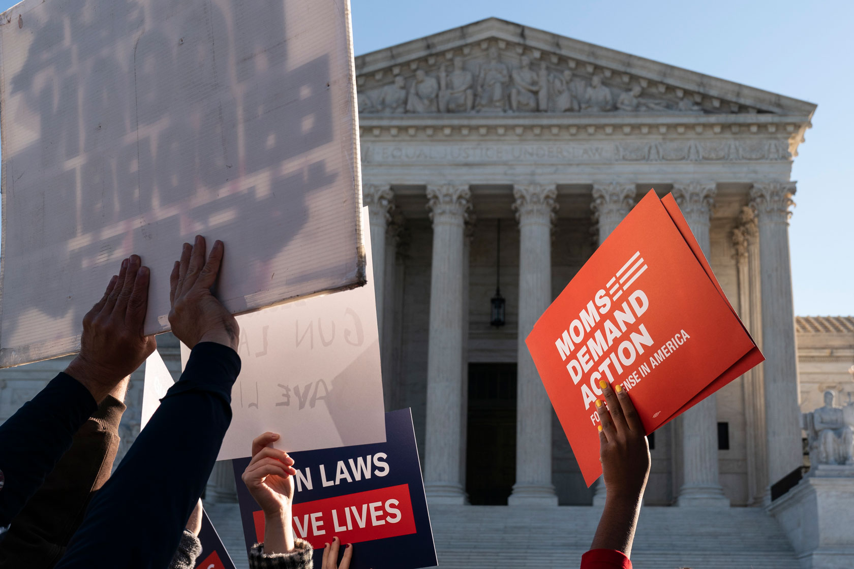 Protestors' hands hold up signs promoting gun regulation in front of the Supreme Court.