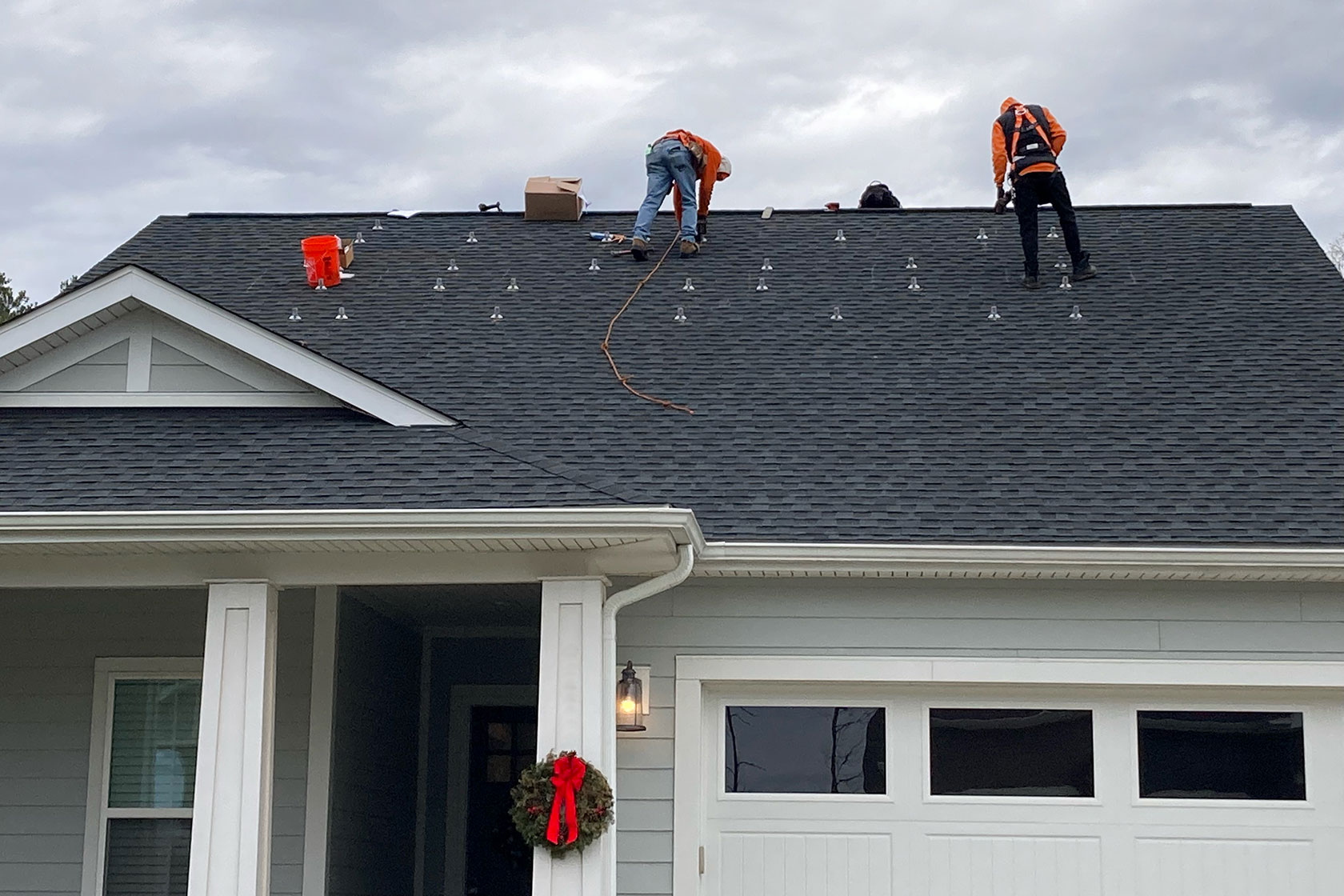 Photo shows workers on a roof of a light grey hours against a cloudy sky