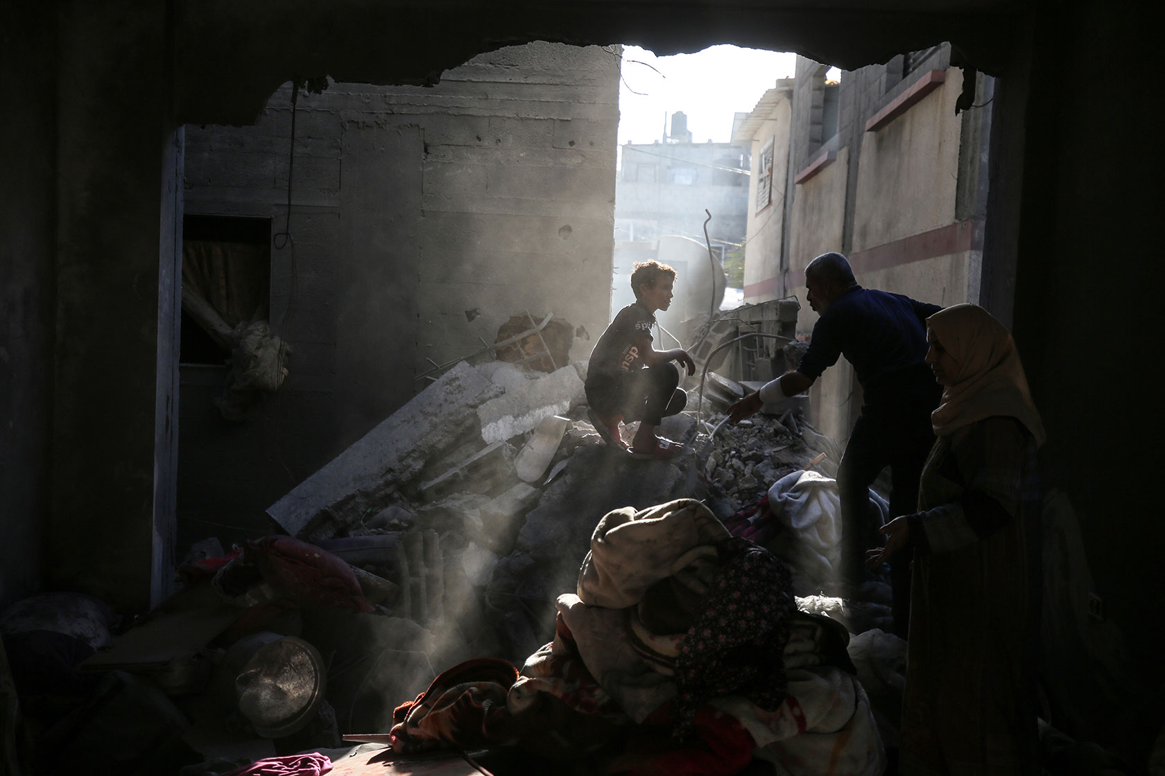 Photo shows a father reaching for his young child sitting on top of rubble in the destroyed home, with an opening in the wall letting in a stream of sunlight