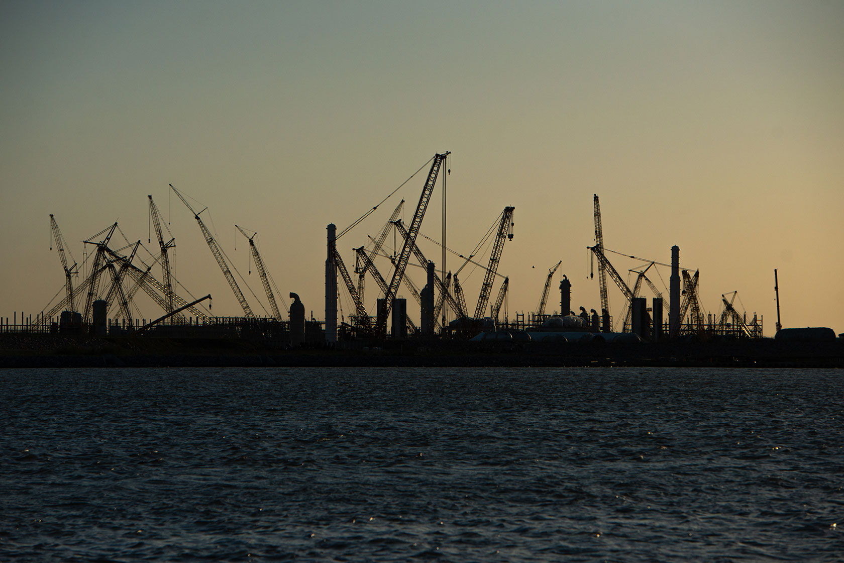 Construction cranes stand silhouetted by the sunset at the Golden Pass LNG terminal.