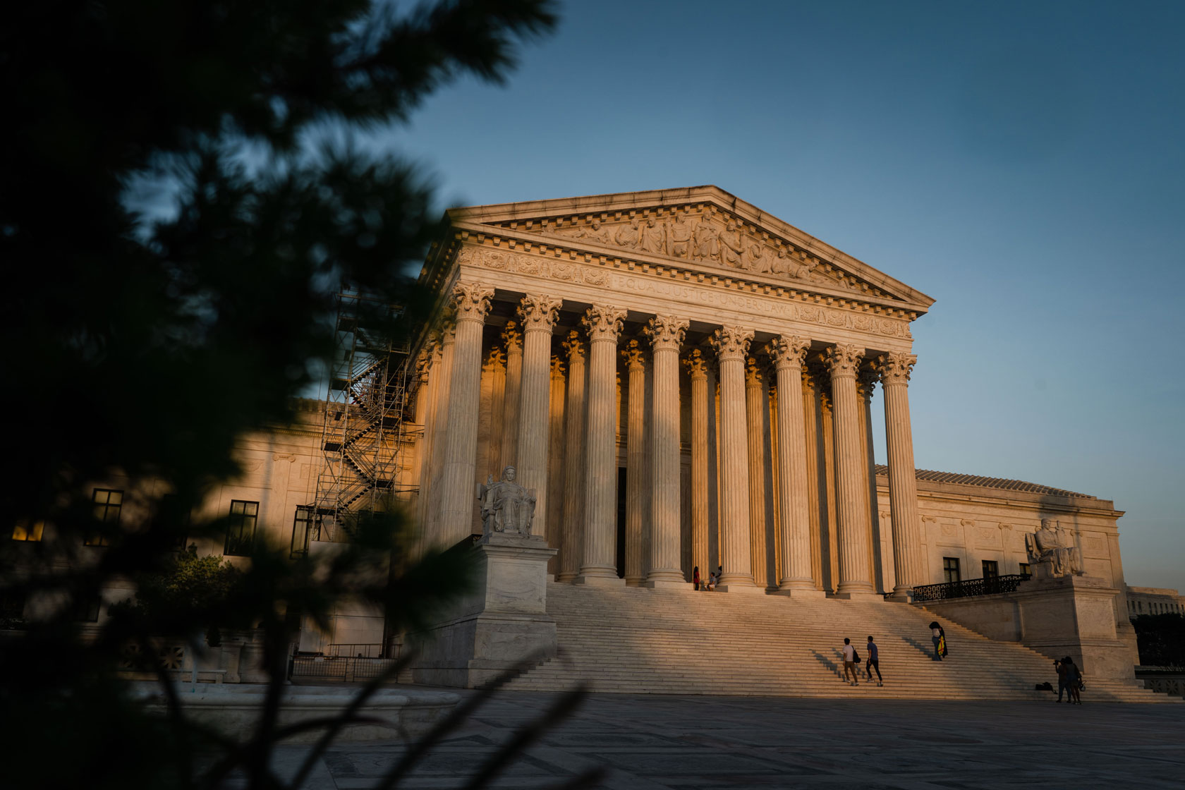 The U.S. Supreme Court building is seen with sunlight shining on it and a tree shadowing the foreground.