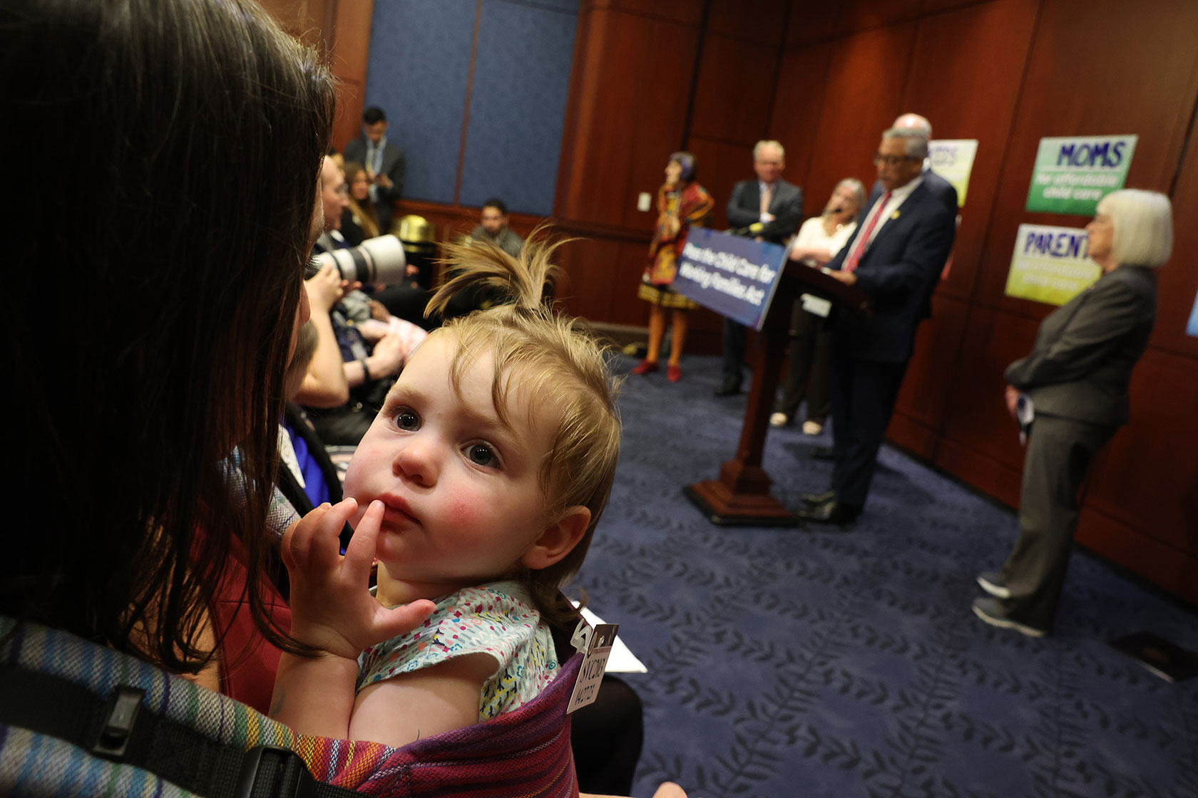 A mother holds her child during an event to reintroduce child care legislation.