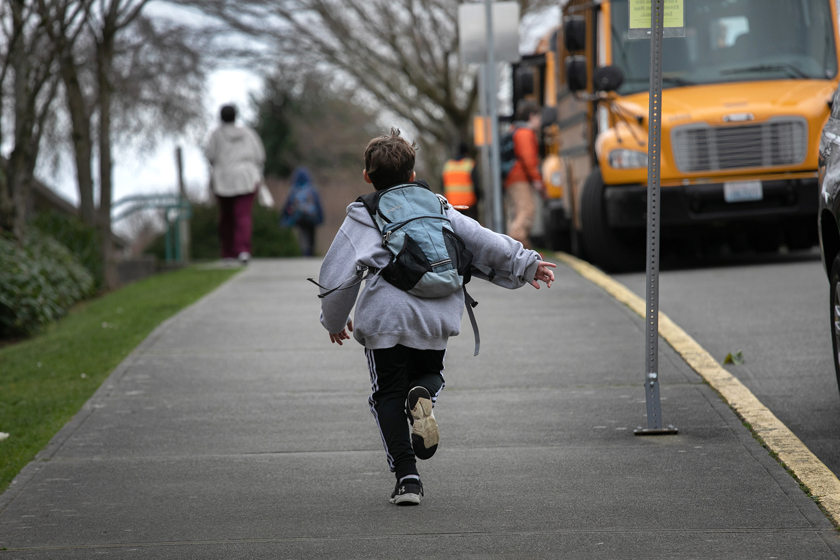 Student running down sidewalk; school bus in distance