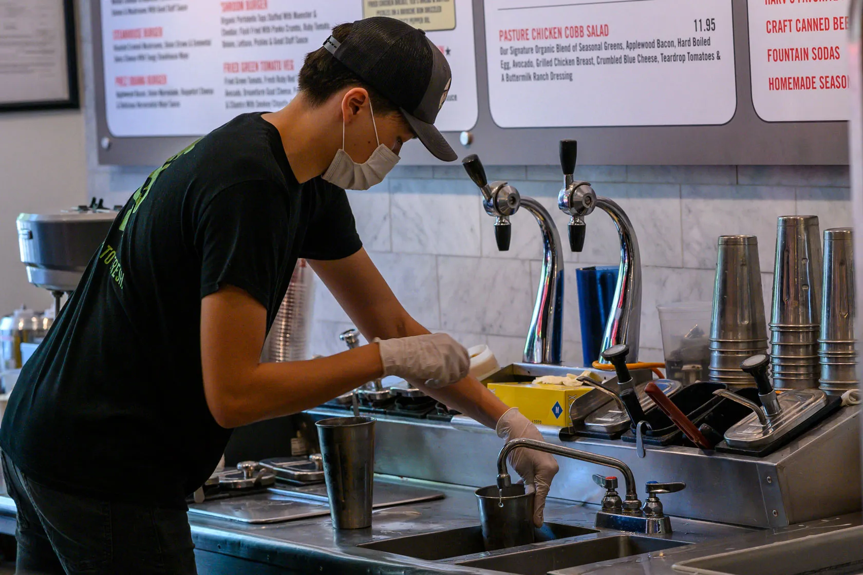 A young man washes cups in a fast food restaurant.