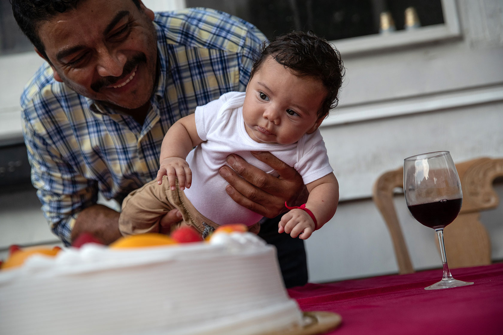 Photo shows a man in a plaid shirt holding a young baby in front of a cake.