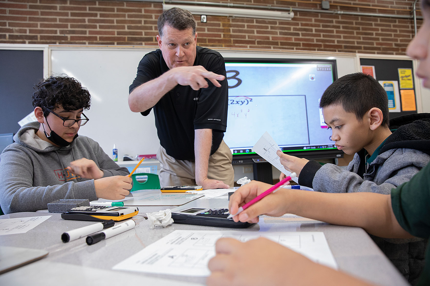 A retired teacher leads a math tutoring session with middle school students.