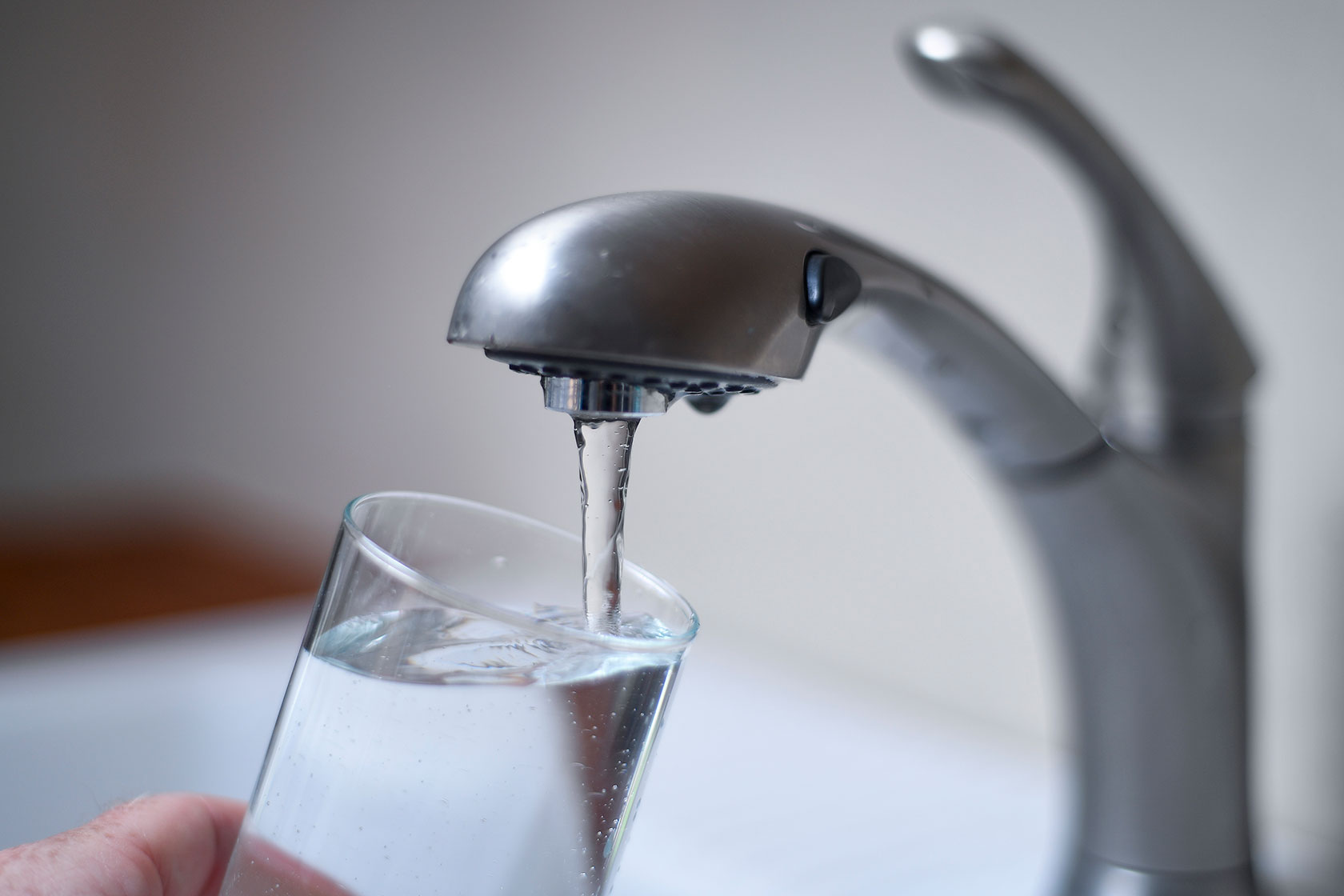 Photo shows a hand holding a clear glass underneath a running faucet