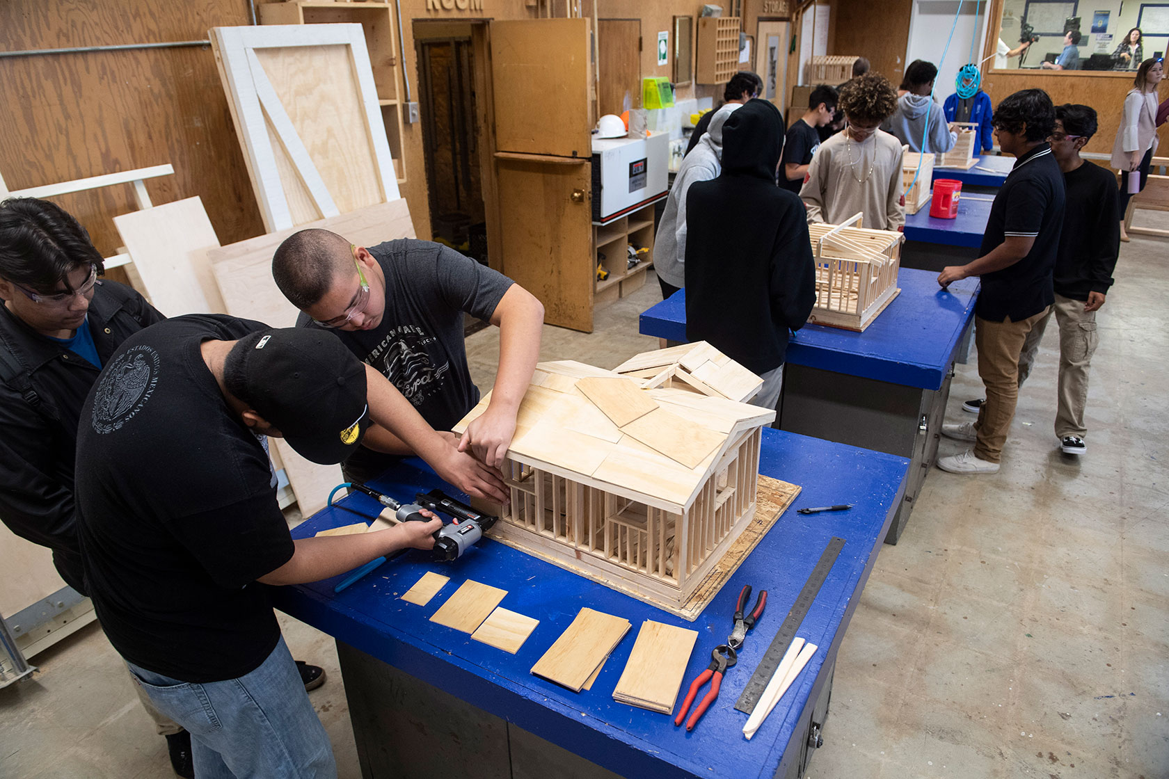 Photo shows a group of students gathered at two tables assembling wooden model homes