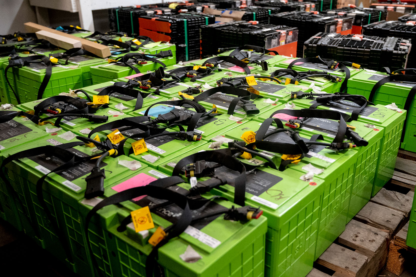 Stacks of green used electric vehicle batteries sit on the floor of a factory.
