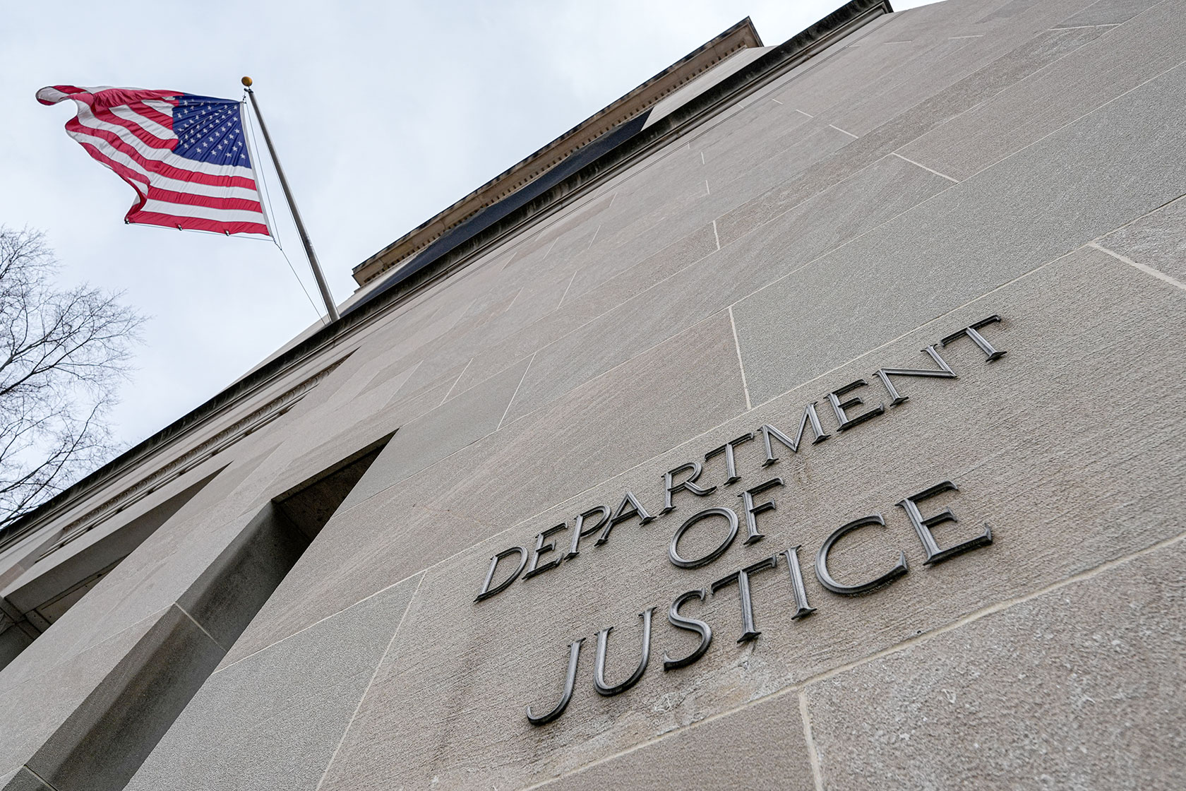 Photo shows an upward shot of the U.S. flag, and beneath it, text affixed to the side of a building that reads 