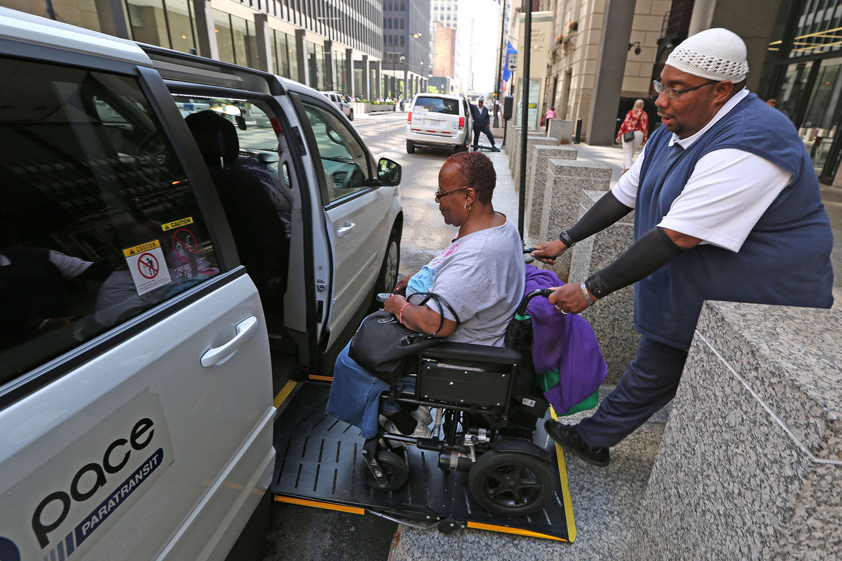 Photo shows a man pushing a woman in a wheelchair into a van