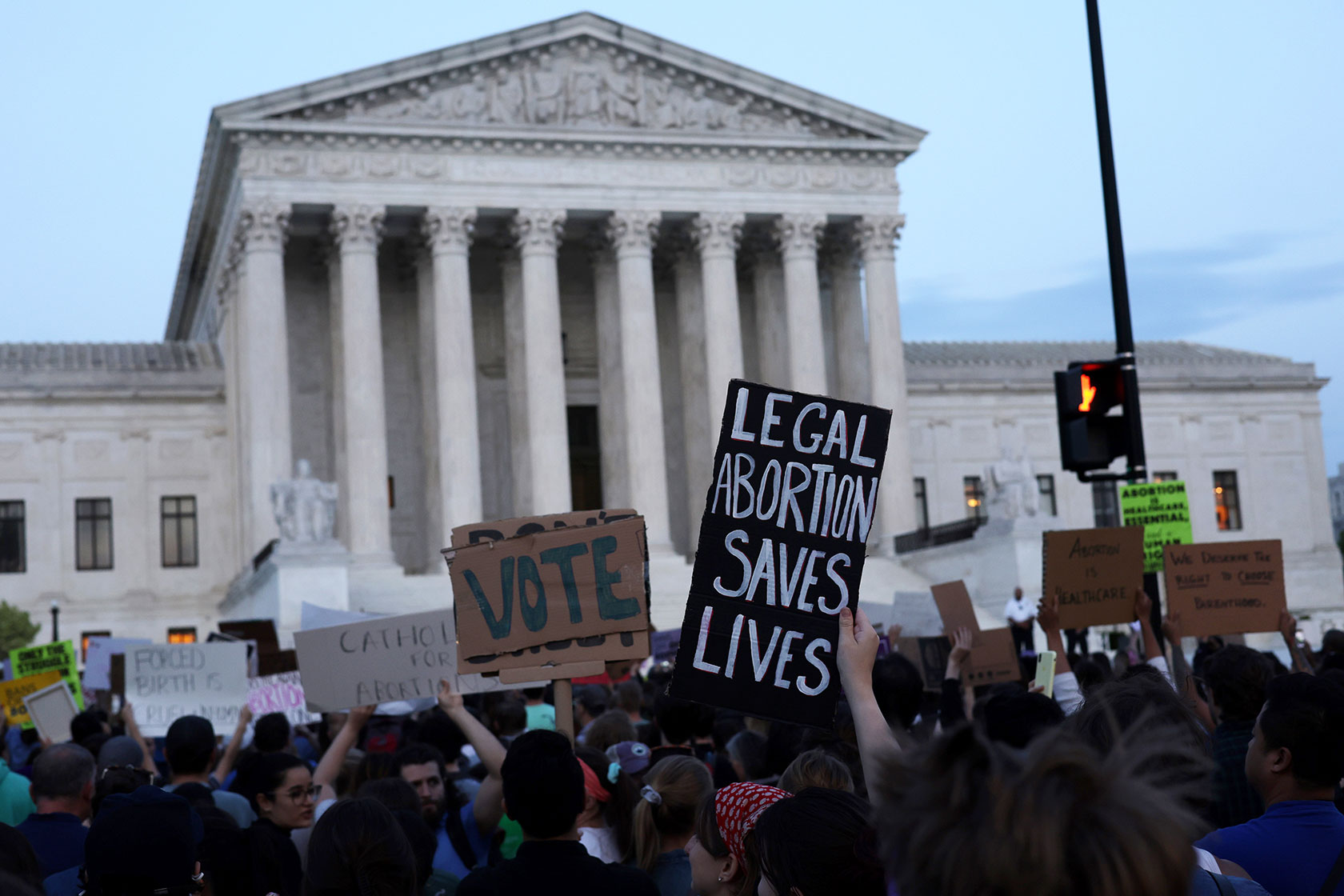Photo shows a group of people demonstrating in front of the Supreme Court building. One sign reads 