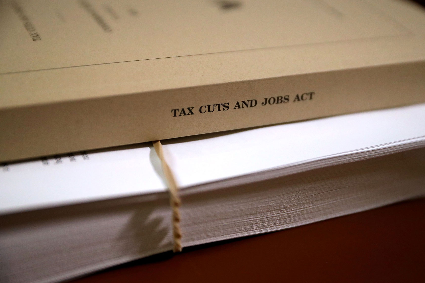 Photo shows a bound copy of the Tax Cuts and Jobs Report conference report atop a stack of loose papers held together with a rubber band.